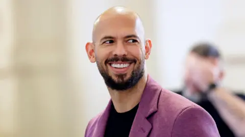 EPA Photograph of Andrew Tate smiling and wearing a purple blazer