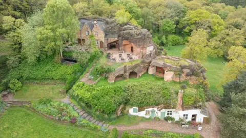 National Trust An overhead drone shot showing homes built into the side of a hill with doors and windows cut into the sandstone. Some openings of caves can be seen.