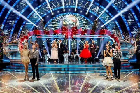 The contestants of the Christmas special standing on the stage clapping and smiling.