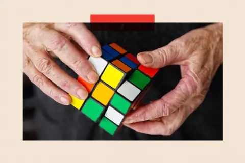 Getty Images An elderly persons hands move a cube