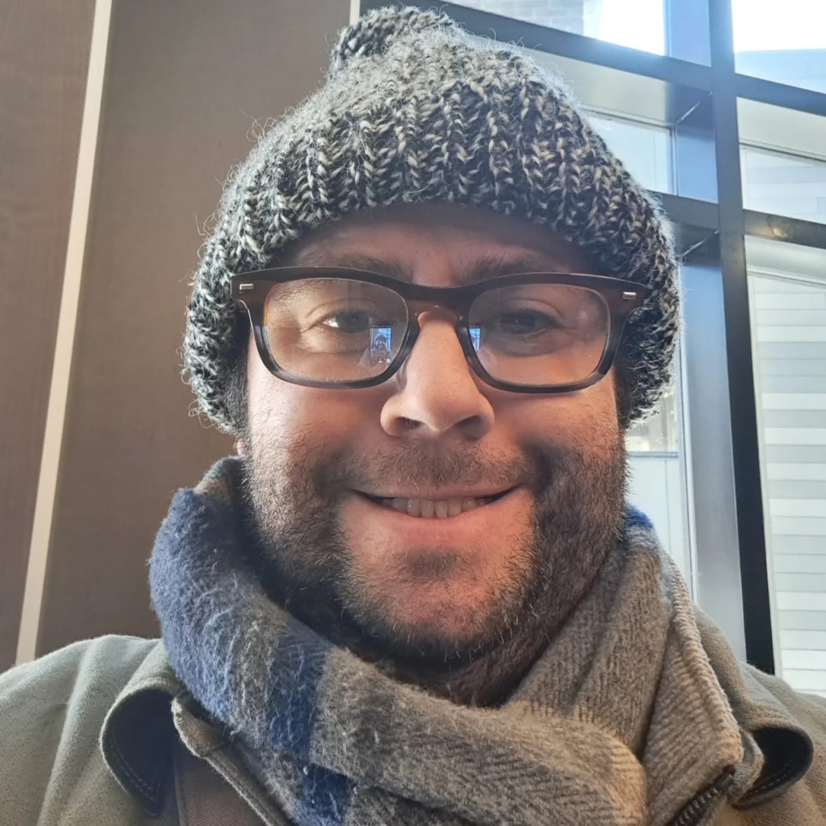 A man with a beard, glasses and a winter hat smiles for the camera.