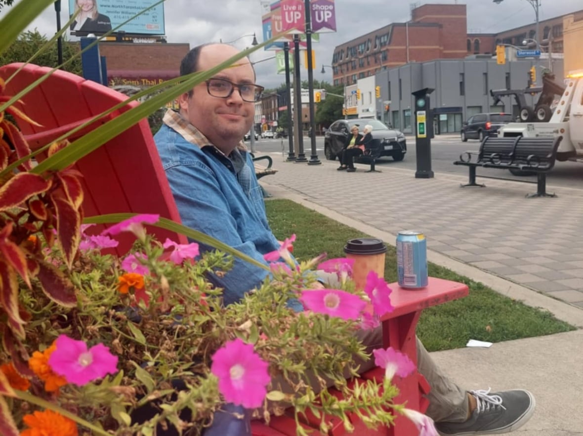 A man sits on a red chair near flowers.