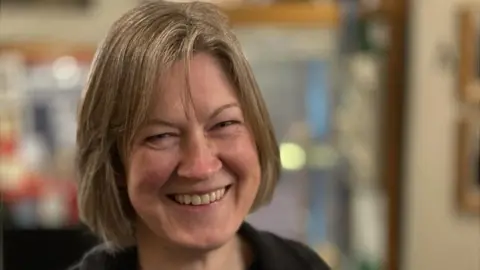 Helen Geake who has short, bobbed, light brown hair. She is wearing a dark top and is smiling towards the camera