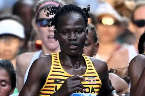 Reuters Rebecca Cheptegei takes part in a race wearing a yellow top with black and red stripes.