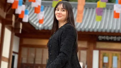 Mary Gedda Mary Gedda, dressed in black, smiles in a photo taken in Seoul. A wooden building with a tin roof can be seen behind her