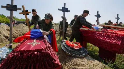 Reuters Several Russian soldiers pin flags to coffins of soldiers killed in Luhansk, Russia-controlled territory, surrounded by crosses