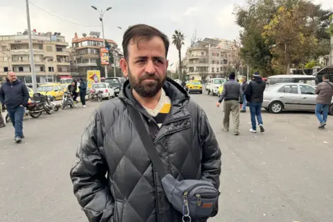 Aamir Peerzada/BBC A man wearing a black padded jacket stands on the street in Damascus.