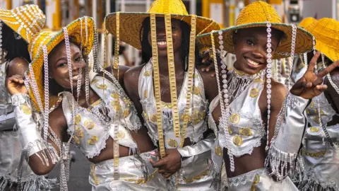 Olympia De Maismont / AFP Women in silver outfits and gold-brimmed straw hats with chains hanging from their smile as they pose for the camera in Calabar, Nigeria