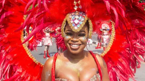 Emmanuel Adegboye / EPA A woman taking part in Calabar's carnival smiles as she wears a massive red feathered headdress