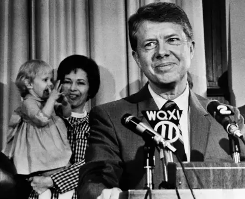 AP Former State Sen. Jimmy Carter listens to applause at the Capitol in Atlanta on April 3, 1970, after announcing his candidacy or governor.  In background, his wife Rosalyn holds two-year-old daughter Amy who joined in the applause. 