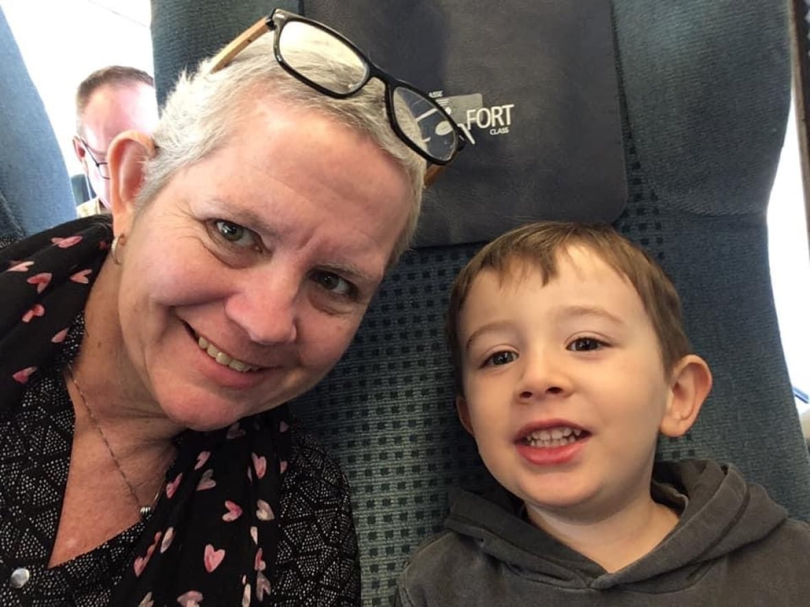 A woman with short hair takes a selfie with a young boy on a train.