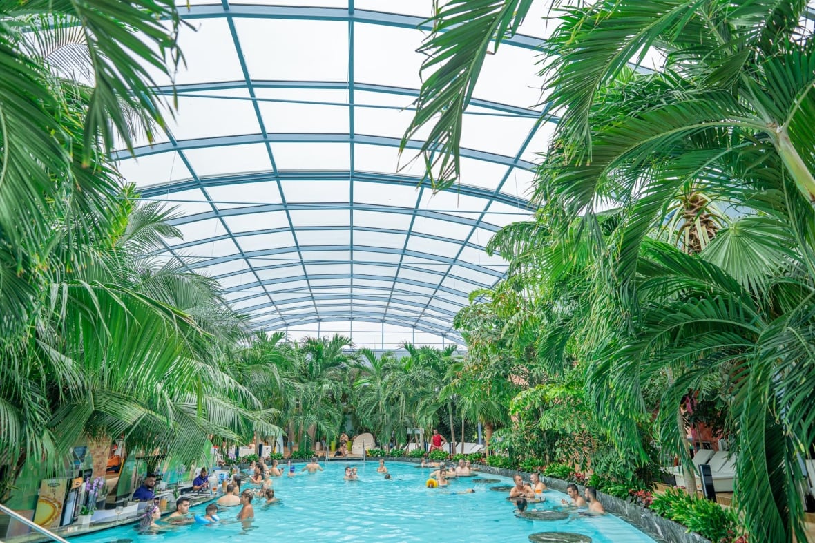 This rendering by Therme Canada shows an indoor pool full of people with plants and palm trees lining the circumference.