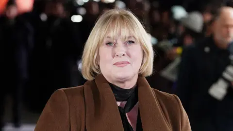 PA Media Sarah Lancashire at an outside event. She has blonder hair to her shoulders and is wearing a brown coat.