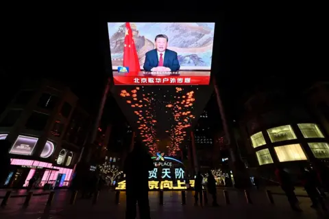 ADEK BERRY/AFP A large screen shows Chinese President Xi Jinping delivering a speech ahead of the New Year's eve celebrations in Beijing on December 31,