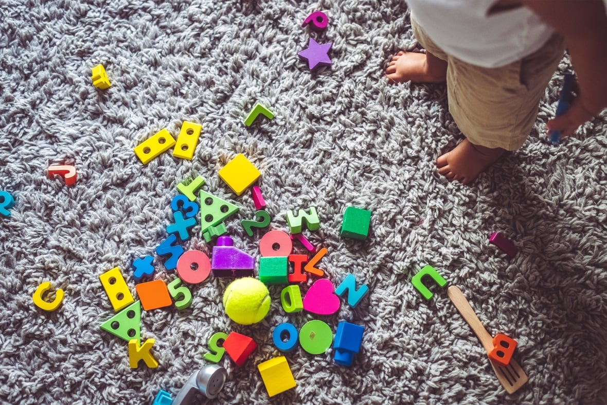 Child looking down on a carpet full of toys