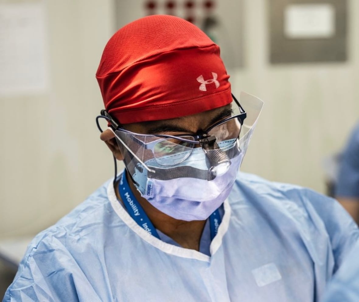 A man wearing a medical mask and scrubs with a doctor's headlamp on his eyeglasses.