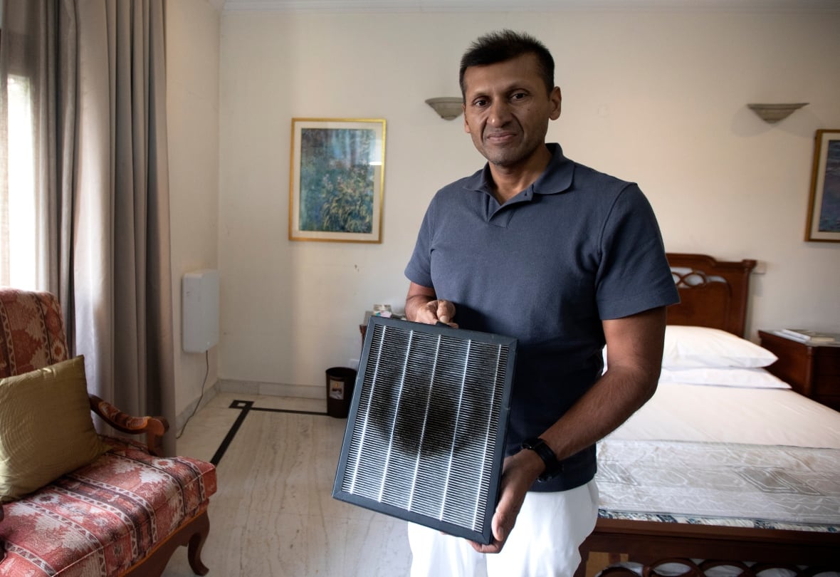 A man holds the blackened square filter from an air purifier.