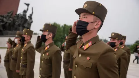 Getty Images North Korean soldiers wearing facemasks salute as they pay their respects to the country's former leaders in 2021