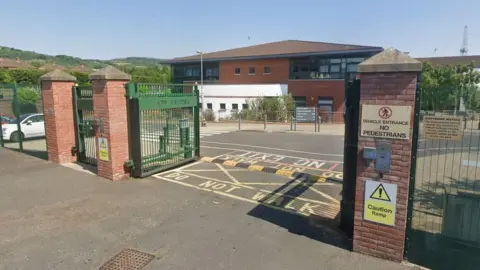 Google The gates of a school, with the school building in the background. 