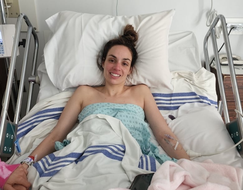 A woman smiles while lying in a hospital bed with IVs in both arms. 