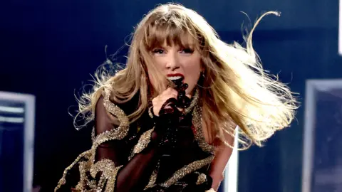 Getty Images Taylor Swift on stage in Vancouver, wearing a black outfit braided with gold bands