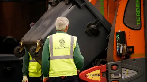 Getty Images A bin lorry collects rubbish, flanked by two collectors wearing high-vis vests, in Stoke-on-Trent