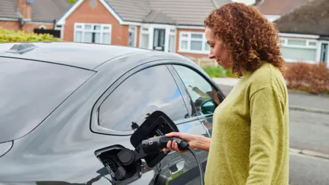 Getty Images Woman charging an electric car parked on her drive