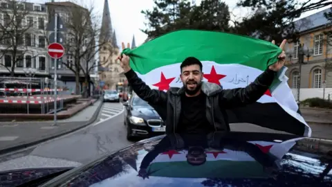 Reuters A man holds a Syrian flag in a car in Germany as he celebrates the downfall of Bashar al-Assad in his home country