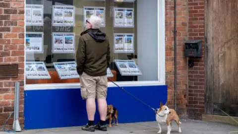 Getty Images Man looks at house prices in a shop window while walking his two dogs