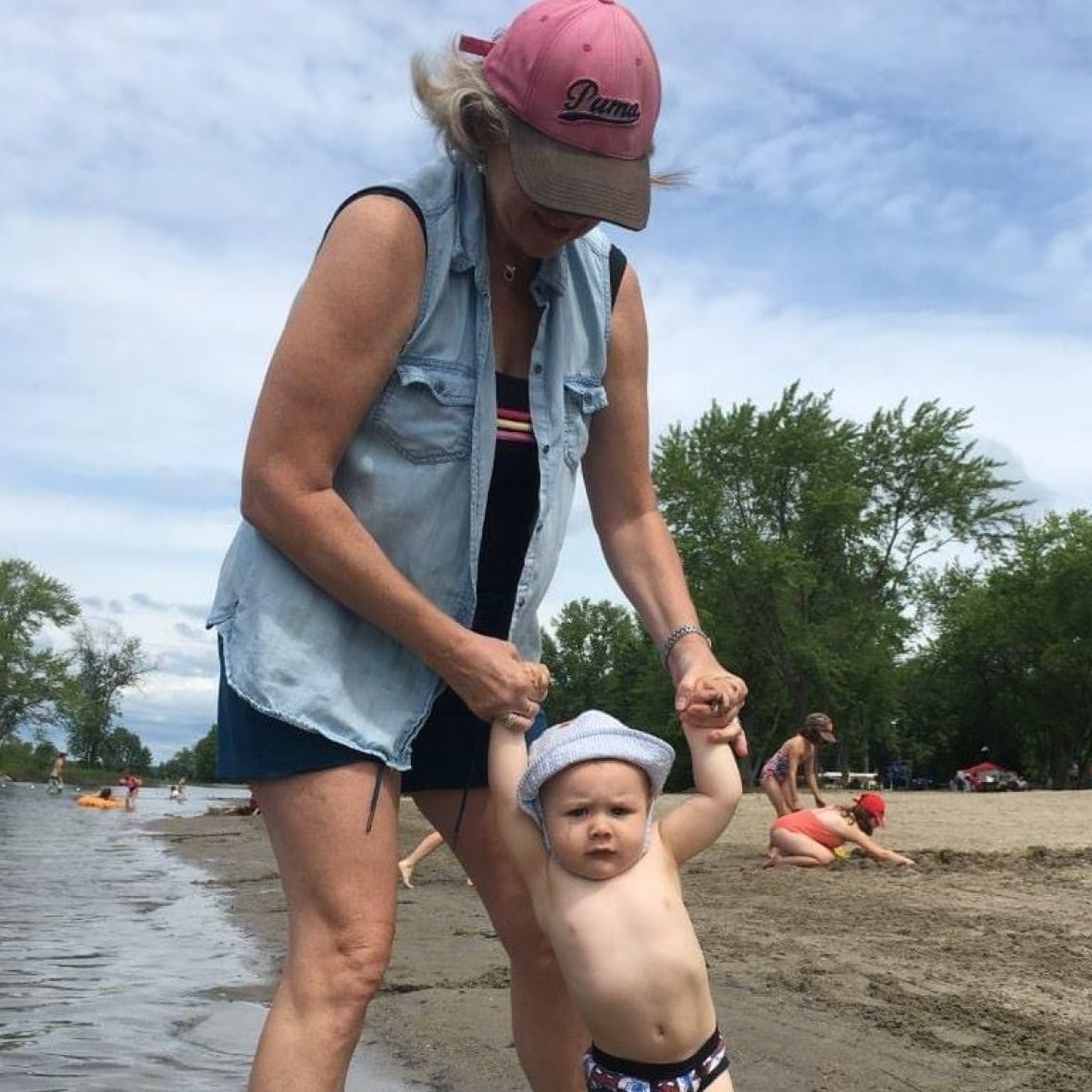 A woman holds a young boy's arms at a beach.