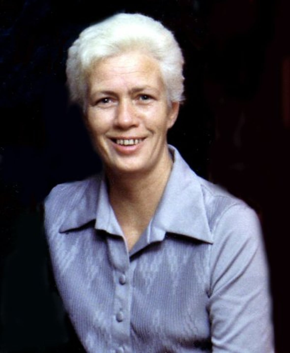 An older photo of a woman with white hair and a purple shirt.