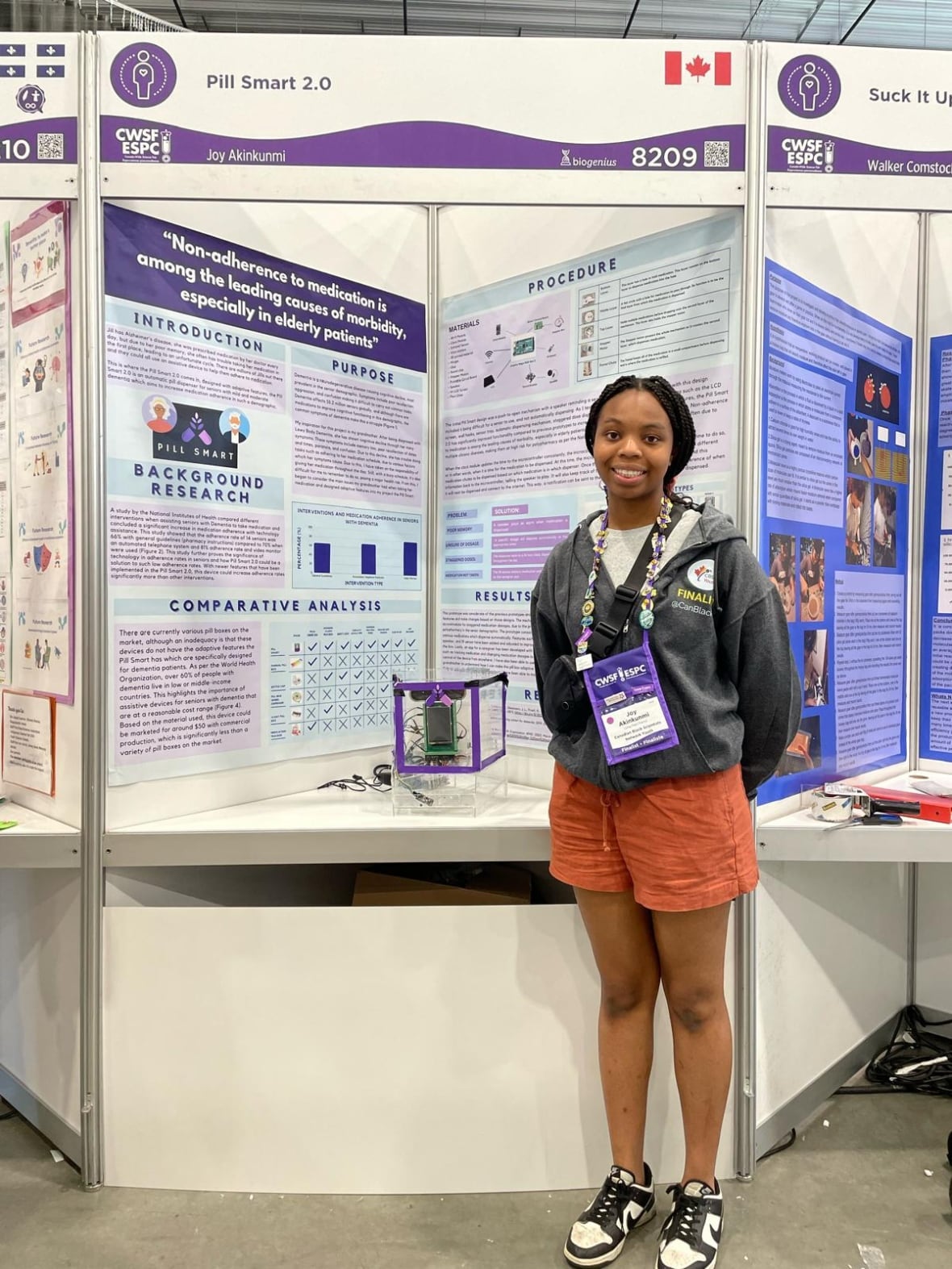 A smiling Black teenage girl is shown at a science fair showing off her device.