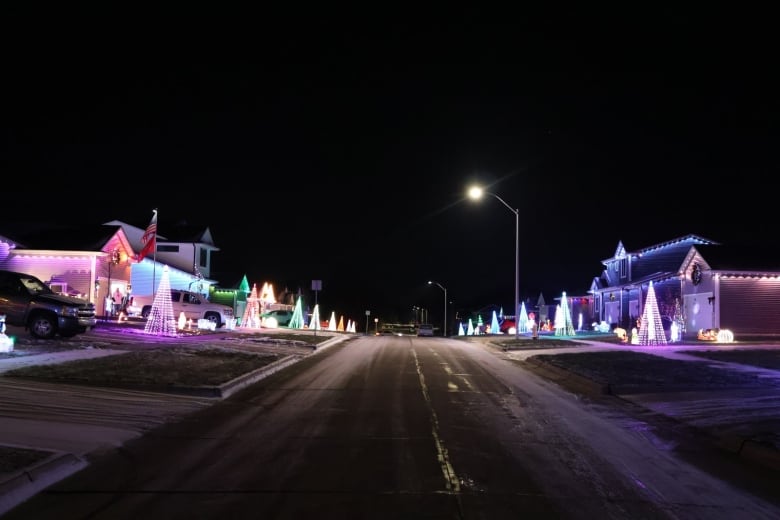 A snow-lined street at night with Christmas lights and trees on every house