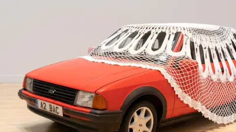 Keith Hunter A red car with a doily over, part of Jasleen Kaur's exhibition