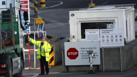 EPA A woman dressed in a high visibility jacket and vest has her hand outreached to gather documents from a lorry driver.