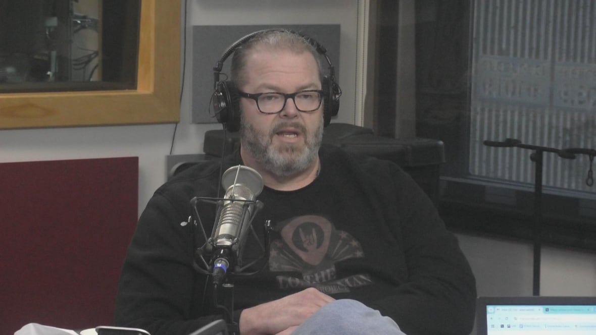 A man wearing headphones sits next to a microphone.