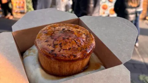 Tommy Banks Pie and mash, covered with gravy, in a cardboard takeaway box.