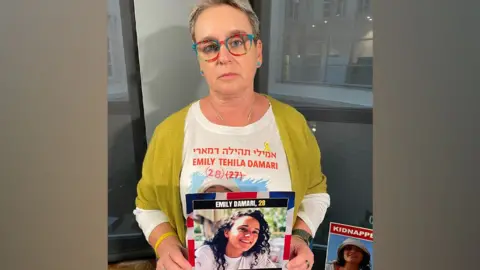 BBC Mandy Damari holds up a photo of her daughter Emily Damari, who is being held hostage by Hamas in the Gaza Strip, during a visit to the UK (3 December 2024)