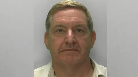 Gloucestershire Police Police mugshot of offender Ashley Watson in custody wearing a pale yellow shirt and looking at the camera