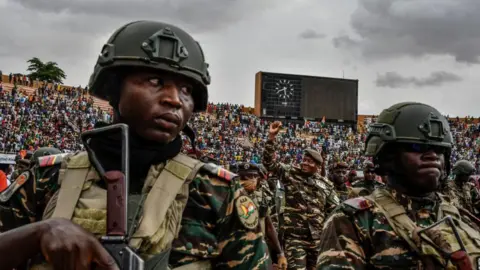 AFP Flanked by troops, Niger's coup leader Gen Abdourahamane Tchiani (C) greets the thousands of people at a  stadium in Niamey on 26 July 2023. They are all wearing camouflage.