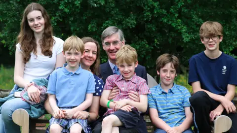 Discovery+ Jacob Rees-Mogg pictured on a bench with his wife and five of his kids 