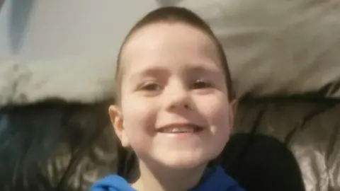 Family handout Kyran Durnin smiles while looking directly at the camera. He has short brown hair and brown eyes. Kyran is sitting on a brown leather couch which has a white blanket draped in the background. He is wearing a blue hoodie.