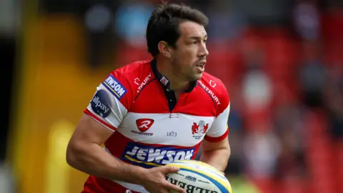 Action Images Tom Voyce playing for Gloucester, wearing a red and white shirt and carrying a ball.