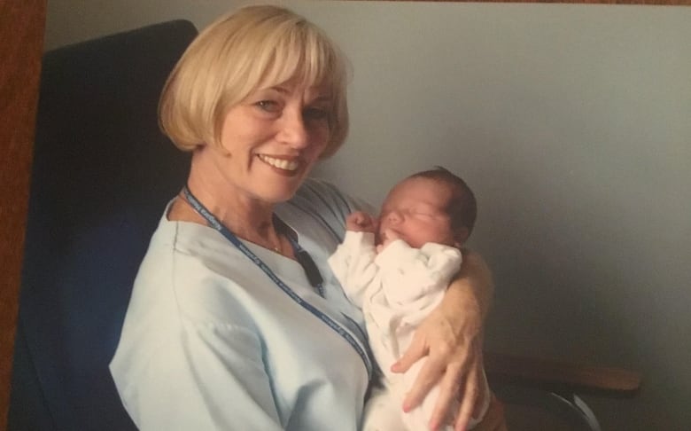 Woman in blue nurse scrubs hold a baby