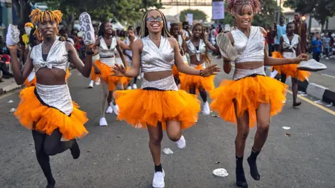 Olympia De Maismont / AFP Nigeria dancers in silver tops and orange pom pom skirts skip down a street at Calabar's carnival