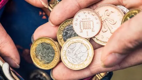 Getty Images Very close up on a hand holding one pound coins as well as one and two pence pieces.