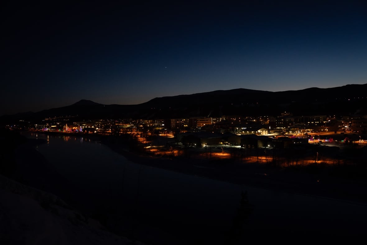 The photo shows a city still in the darkest of the matinee, some buildings and streetlights shining. 