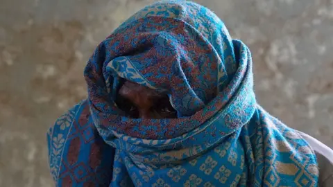 BBC A fisherman-turned-pirate looking directly at the camera through a blue patterned scarf wrapped around his head only allowing his eyes to peep through - Eldoret, Somalia