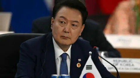 Getty Images South Korea's President Yoon Suk Yeol sits in a meeting in a dark blue suit behind a South Korean flag