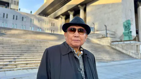 BBC An 80-something South Korean man stands in front of the steps of a large building in Seoul